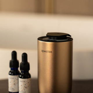 Gold aroma diffuser with 'Aemster' branding next to two dropper bottles on a neutral background